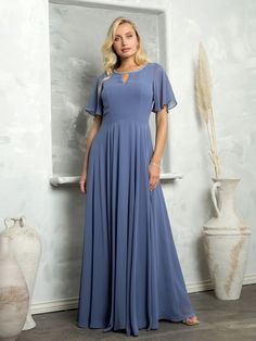 a woman standing in front of a wall wearing a long blue dress with short sleeves