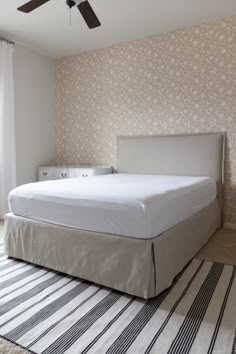 a white bed sitting next to a window with a ceiling fan on top of it