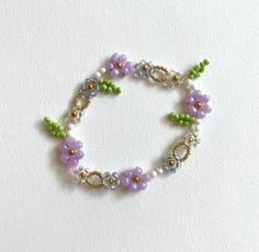 a beaded bracelet with flowers and leaves on it's end, sitting on a white surface