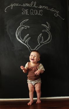 a baby sitting in front of a blackboard with writing on it