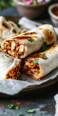 two burritos on a plate with sauce and cilantro in the background