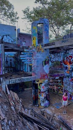 an abandoned building with graffiti all over the walls and roof, along with a woman standing in front of it