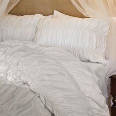 an unmade bed with white comforter and pillows on it's headboard