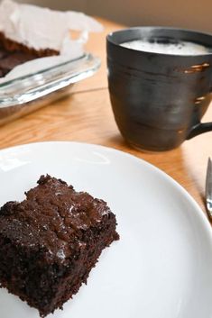 a piece of chocolate cake sitting on top of a white plate next to a cup of coffee