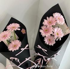 two black vases with pink daisies in them and ribbons tied around the top