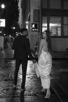 a man and woman walking down the street in the rain at night, holding hands