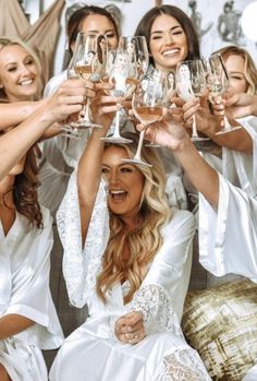 the bridesmaids are all dressed in white robes and holding up wine glasses together