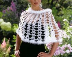 a woman wearing a white crochet shawl in front of some pink flowers