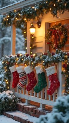 christmas stockings hanging on the front porch with lights and garlands around them, all covered in snow