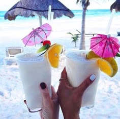 two people holding up drinks on the beach with umbrellas in the sand behind them