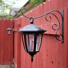 a red fence with a light hanging from it's side and the words, must do solar lights on plant hook - love this idea back yard