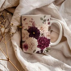 a coffee mug with purple and white flowers on it sitting on top of a bed