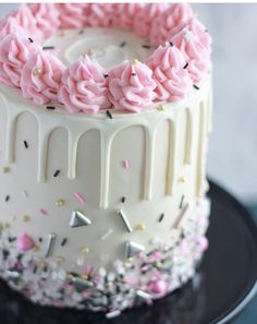 a white cake with pink frosting and sprinkles on a black plate