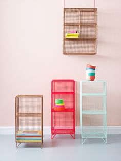 three different colored metal shelves against a pink wall