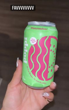 a woman holding up a can of soda with pink and green designs on the side