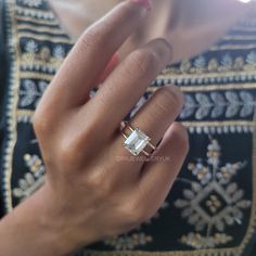 a close up of a person wearing a ring with an emerald stone in the middle