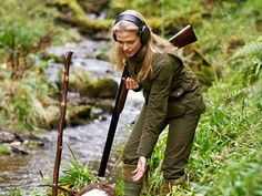 a woman is standing in the grass near a stream and holding a stick with her right hand