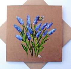 a card with blue flowers and a bee on it's back, in front of a brown envelope