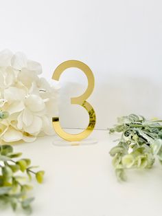 the number three is next to some white flowers and greenery on a white surface