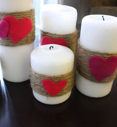 three white candles with red hearts on them and twine wrapped around the candle holders