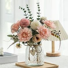 a vase filled with pink and white flowers sitting on top of a table next to a lamp