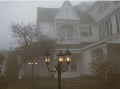 two street lamps in front of a large white house on a foggy day with trees and bushes