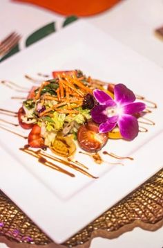 a white plate topped with a salad covered in vegetables and sauce on top of a table