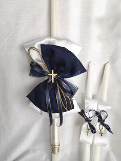 two white candles with blue ribbon and gold cross on them sitting next to each other