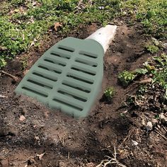 a green plastic grate laying on the ground next to some grass and dirt with weeds growing around it