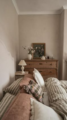 a bed with striped sheets and pillows in a bedroom next to a dresser, mirror and lamp