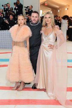 two women and a man standing next to each other in front of photographers at an event