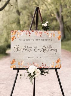 a welcome sign with flowers on it sitting in the middle of a dirt road surrounded by trees