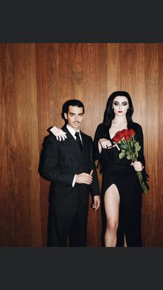 a man and woman dressed in black standing next to each other with roses on their lap