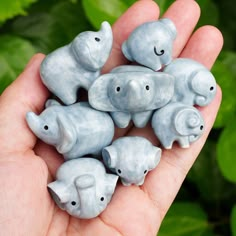 small elephant figurines sitting in the palm of someone's hand with green leaves behind them