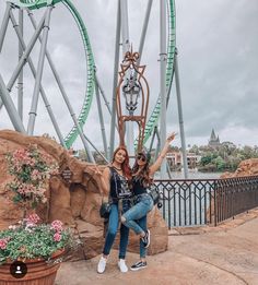 two women pose in front of a roller coaster