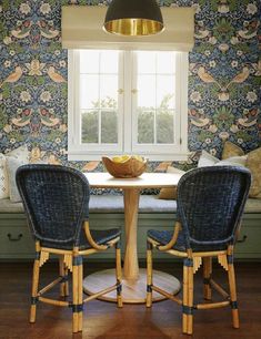 two chairs and a table in front of a window with floral wallpaper on the walls