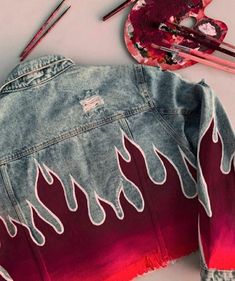 a denim jacket with flames painted on it next to paintbrushes and other art supplies