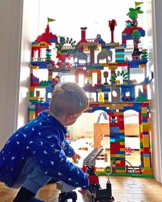 a young boy playing with toys in front of a wall made out of legos