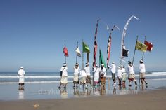 several people are standing on the beach with flags