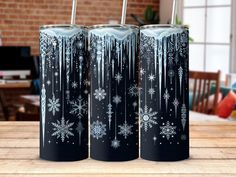 three snowflakes are painted on the side of two black tumblers with straws in them