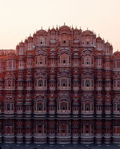 a large red building with many windows on the top and bottom floor, in front of an orange sky