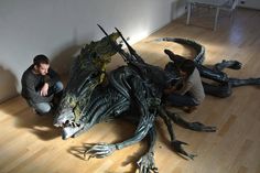 two people sitting on the floor next to a statue of a dragon and another man kneeling down