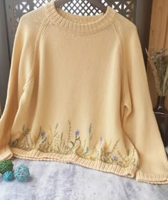 a yellow sweater with flowers on it sitting on a table next to some yarn balls