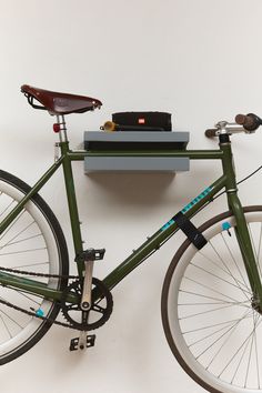 a green bicycle is parked next to a shelf with a bag on it's back