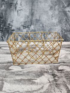 a gold wire basket sitting on top of a gray surface with rocks in the background