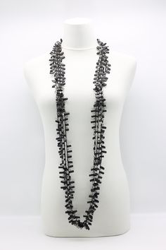 a white mannequin holding a black necklace on it's neck with multiple rows of beads