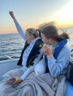 two women sitting on the back of a boat with their arms up in the air