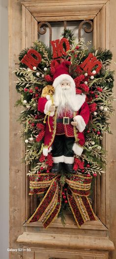 a christmas wreath with a santa clause standing in front of a wooden frame and door