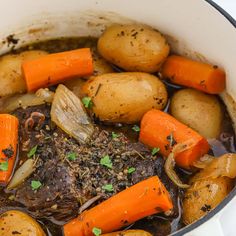 a pot filled with stew and carrots on top of a white countertop next to potatoes