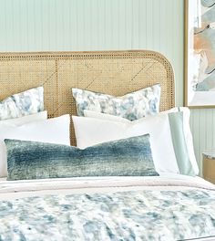 a bed with blue and white pillows on top of it next to a painting hanging above the headboard